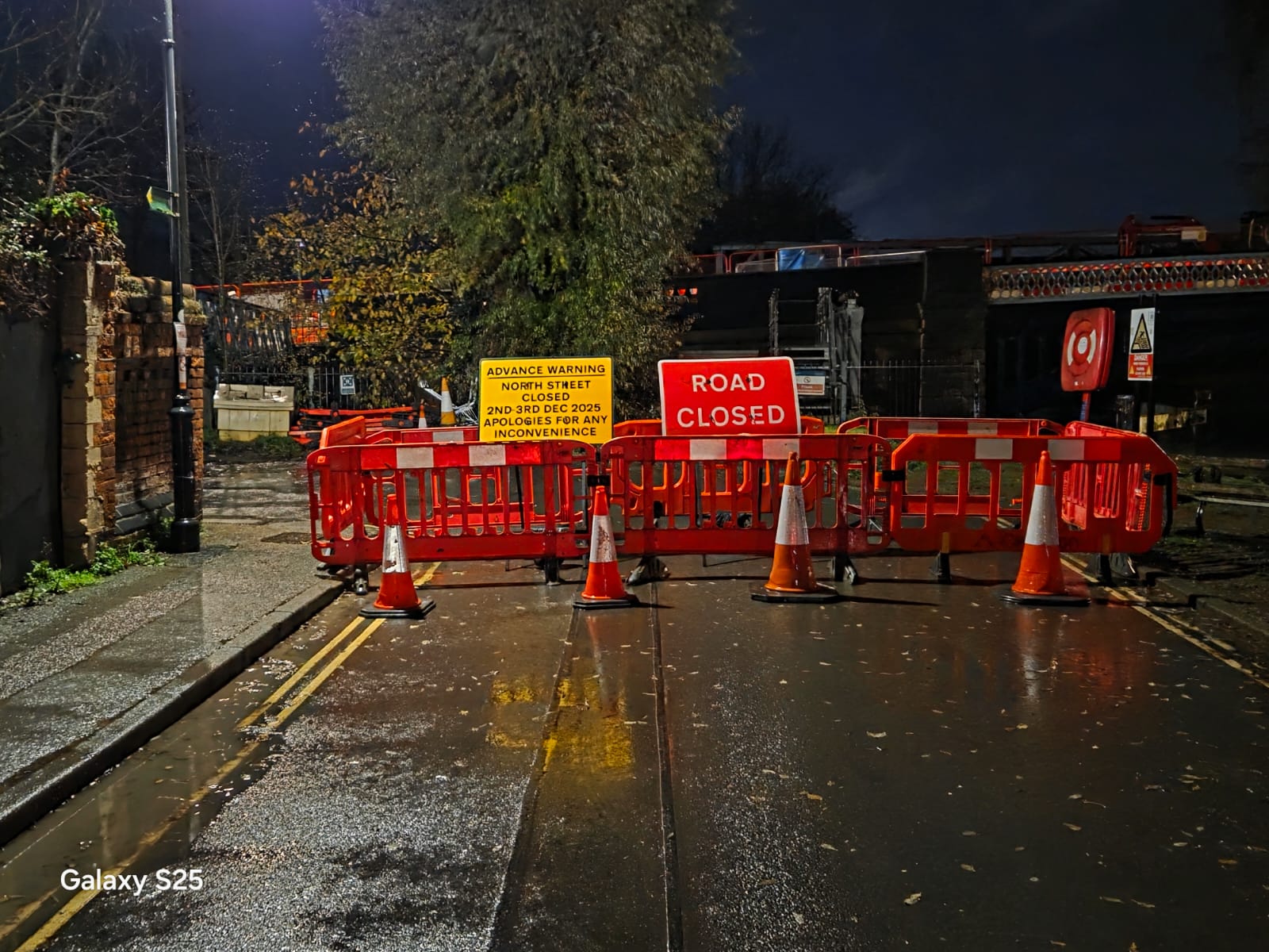 Road closed sign and warning signage on a wet road at night under street lighting
