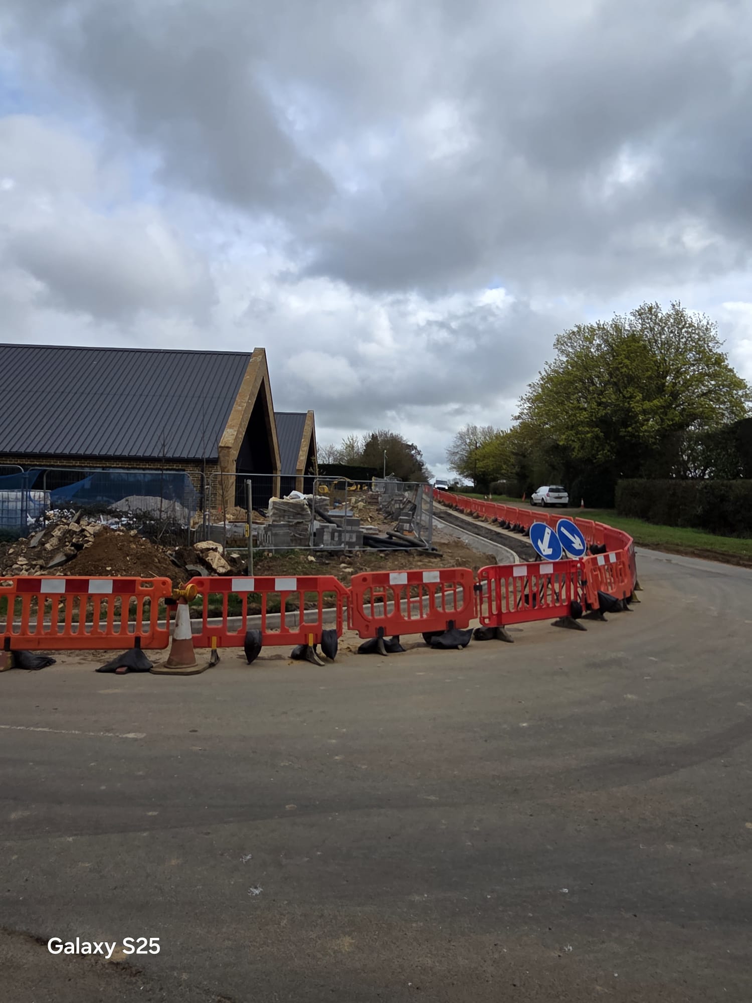 Barriers, cones and keep-left signs guiding traffic around a new kerb line on a low-speed scheme