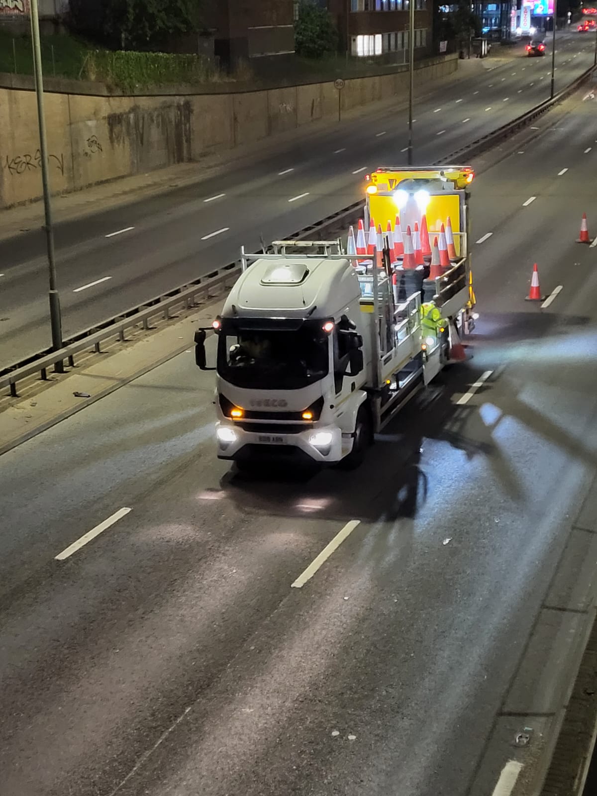 Cone-laden highway maintenance vehicle on a multi-lane road during a night-time lane closure