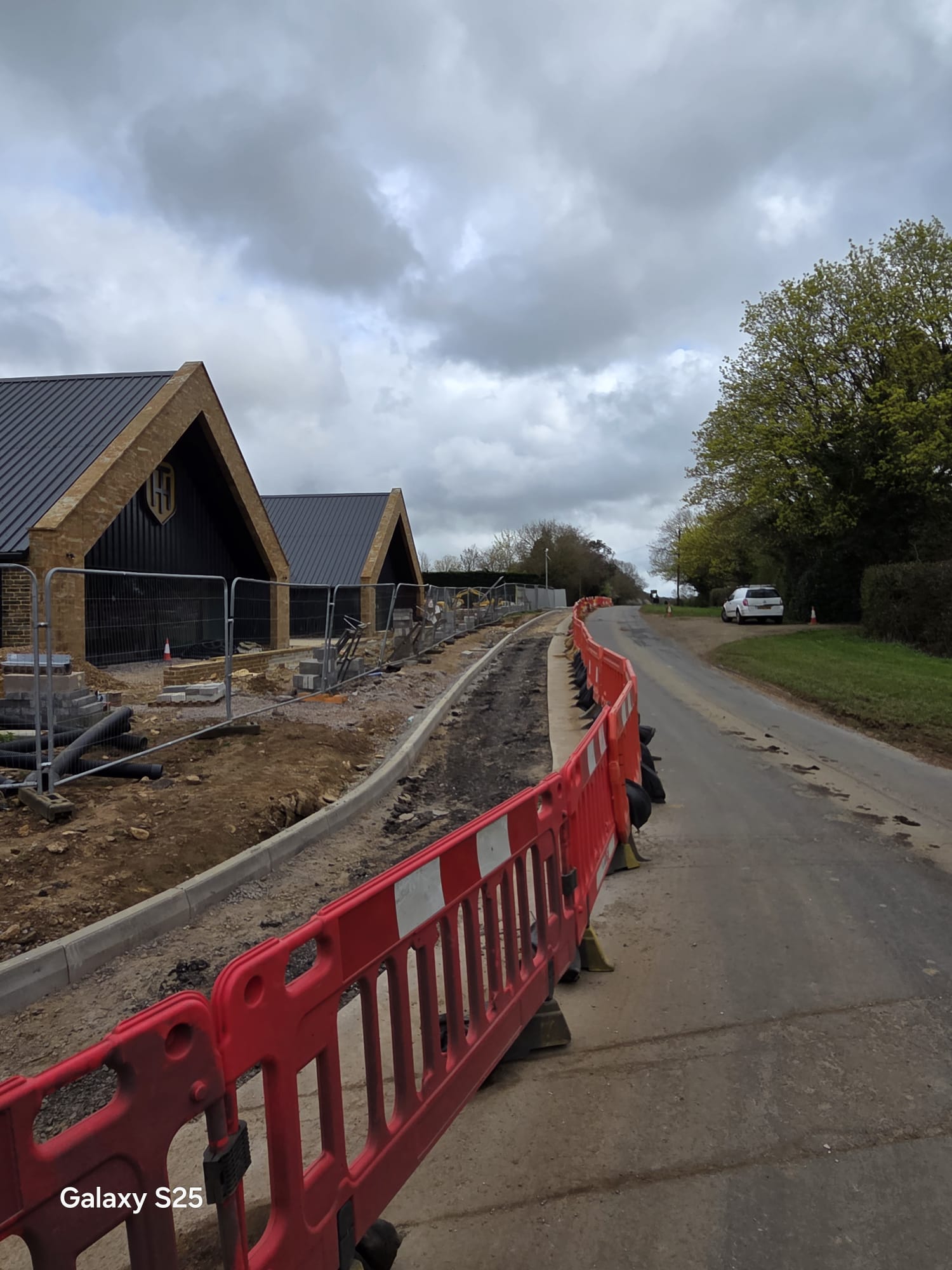 Red barriers separating a live carriageway from construction groundworks on a narrow road