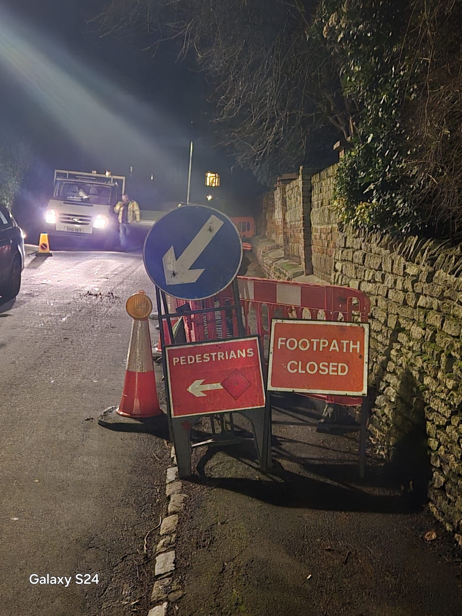 Footpath closed and pedestrian diversion signage lit by works lighting at night