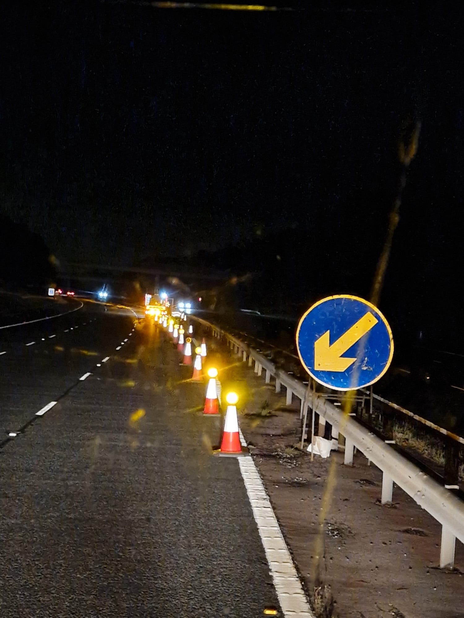 Driver's view of a high-speed lane closure marked by an arrow sign and lit cones