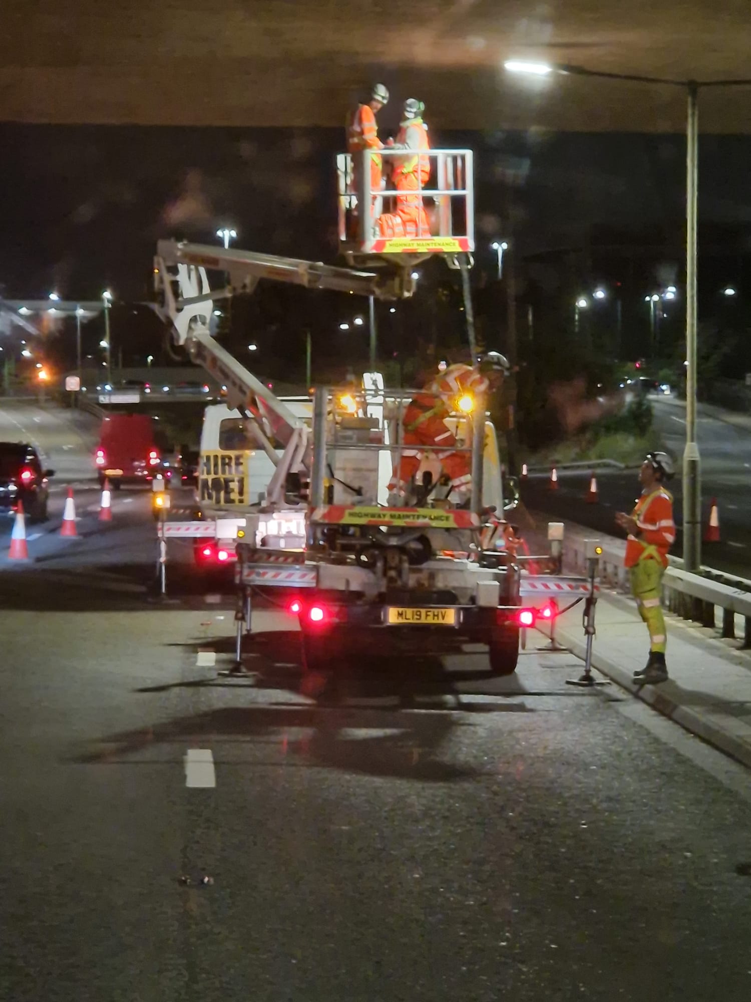 Cherry picker working beneath a bridge at night with traffic management in place