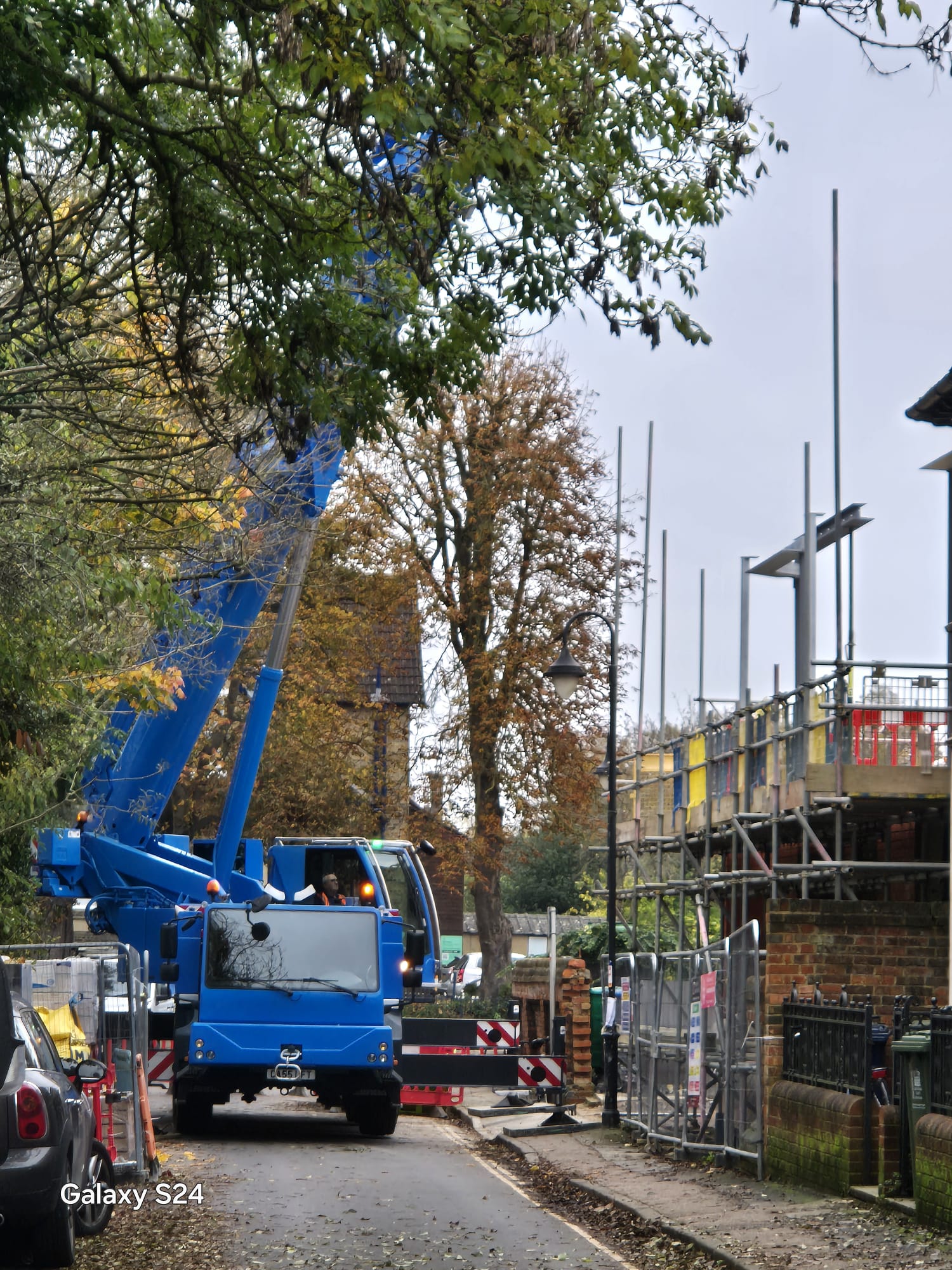Mobile crane lifting beside a scaffolded building on a village street