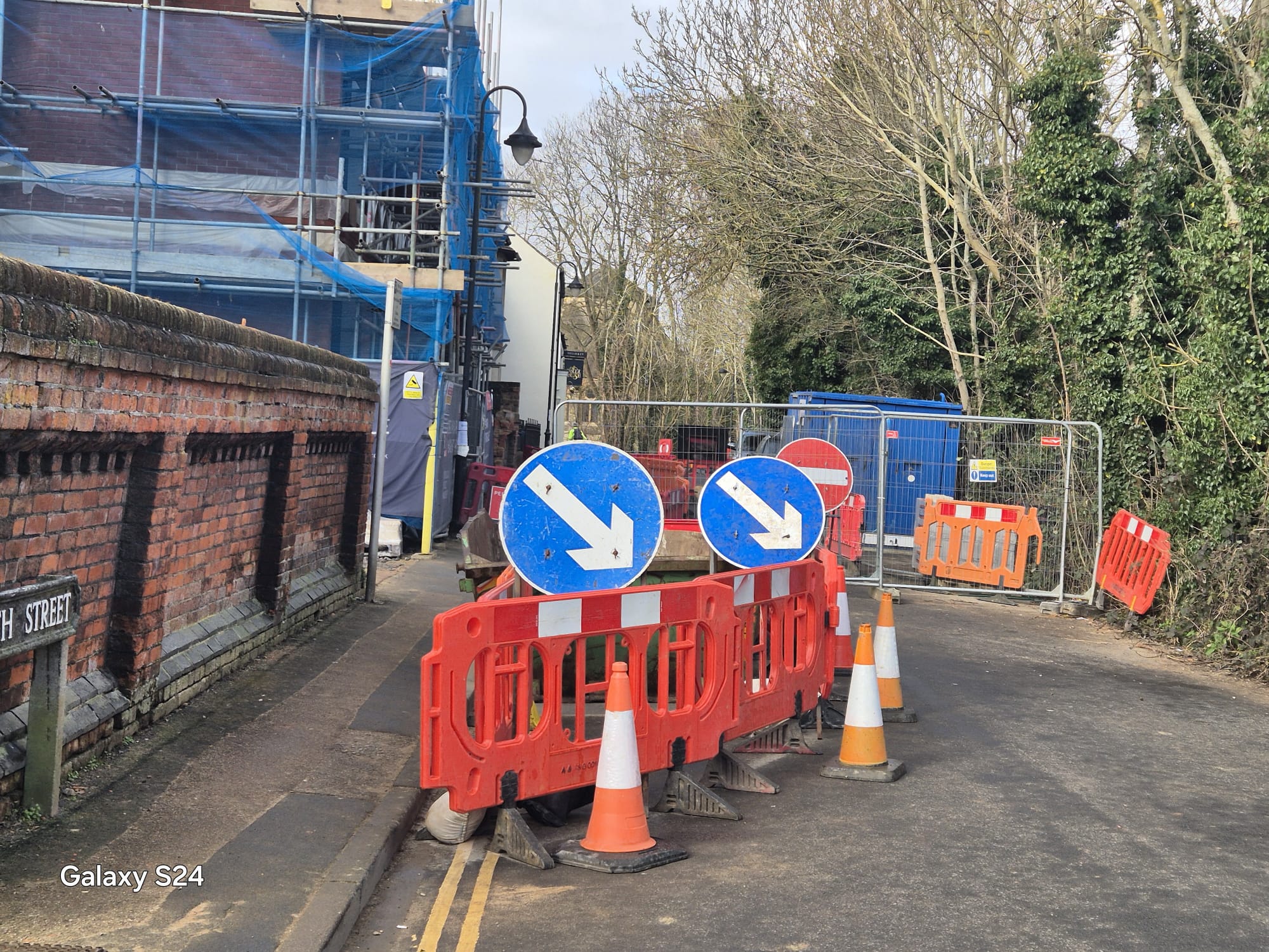 Keep-left arrow signs and barriers closing a street corner beside scaffolding