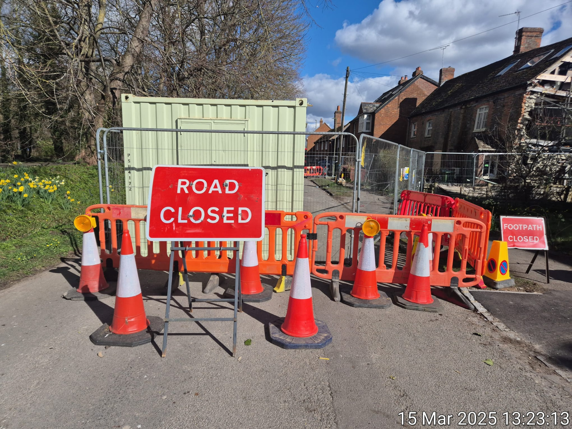 Road closed sign with cones and barriers closing a route beside houses