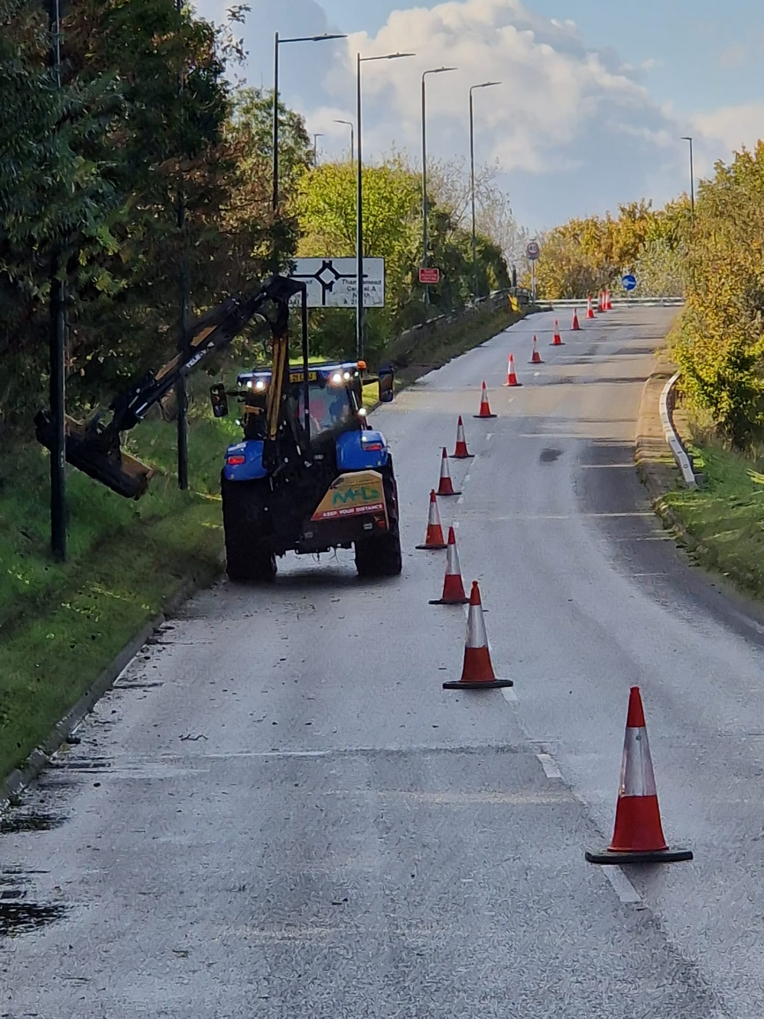 Tractor-mounted verge mowing protected by a coned lane closure on a single carriageway road