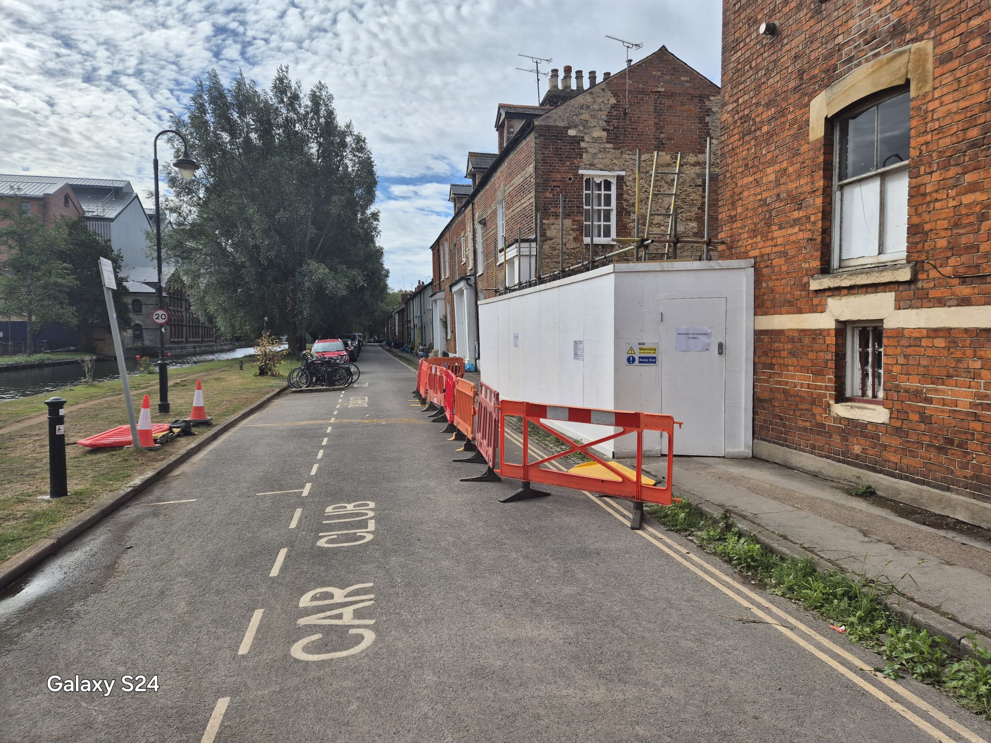 Continuous line of pedestrian barriers separating a closed footway from the live carriageway beside a hoarded site