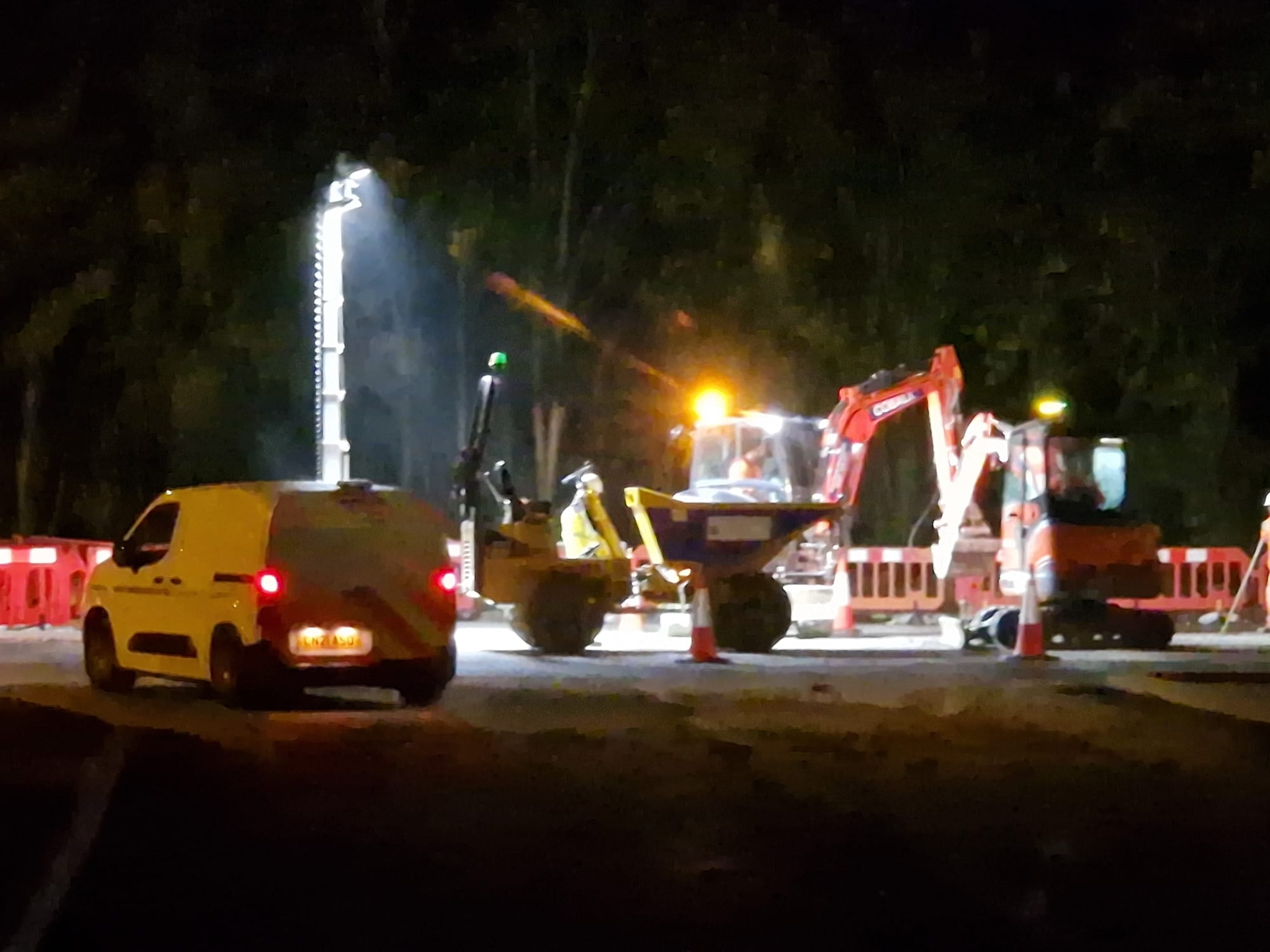 Floodlit night works excavation with plant and works vehicle in attendance
